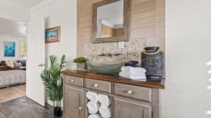 Un bagno con pannelli in mosaico in pietra, un ampio specchio, un lavabo in vetro e un vaso decorativo.