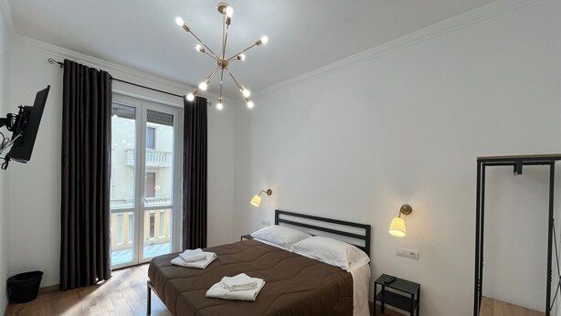 Un dormitorio moderno con una cama grande, una lámpara de techo, una mesita de noche y vistas al balcón exterior.