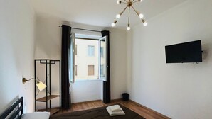 Un dormitorio moderno con una cama grande, una lámpara en el techo, un televisor montado en la pared y una ventana con cortinas.