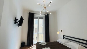 Un dormitorio con una cama, un televisor montado en la pared, una lámpara de techo y una ventana con cortinas.