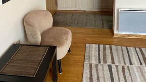 A room with a beige armchair, a wooden floor, a large wardrobe, and a painting on the wall. - Couple Studio PG (Podgorica)