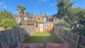 A backyard with a patio area, a small brick building, and a wooden fence.