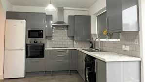 A modern kitchen with grey cabinets, a white refrigerator, a built-in oven, a microwave, a dishwasher, and a pendant light.