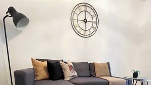 A modern living room with a grey sectional sofa, a woven rug, a wall clock, and a floor lamp.