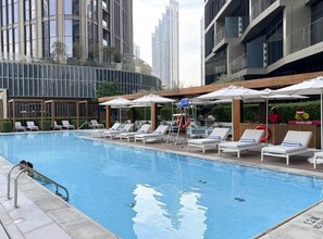 A swimming pool with lounge chairs and umbrellas, surrounded by modern buildings.