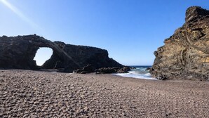 A rocky beach with a natural rock arch formation.