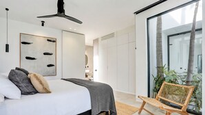 A modern bedroom with a bed, a ceiling fan, a large abstract painting, and a wicker chair.