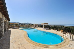 A swimming pool with stone flooring, lounge chairs, and a view of the landscape. - Sunset View Villa in Argaka (Argaka)