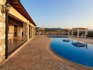 A stone pool with lounge chairs and a pergola, surrounded by stone walls and a wooden deck. - Sunset View Villa in Argaka (Argaka)