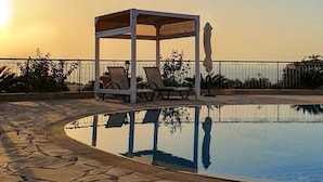 Une piscine dotée d’un belvédère et de chaises longues, entourée d’une terrasse en pierre et d’une clôture en métal.