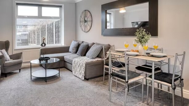 A modern living room with a sofa, a round coffee table, and a dining area with chairs and a table set for breakfast. - Last Min Weekend Stay, Trafford, Pets Welcome (Sale)