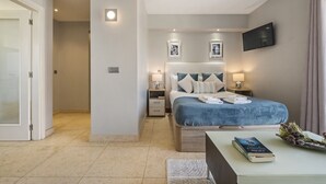 Un dormitorio moderno con una cama grande, mesitas de noche, un televisor de pantalla plana y una puerta que da a otra habitación.
