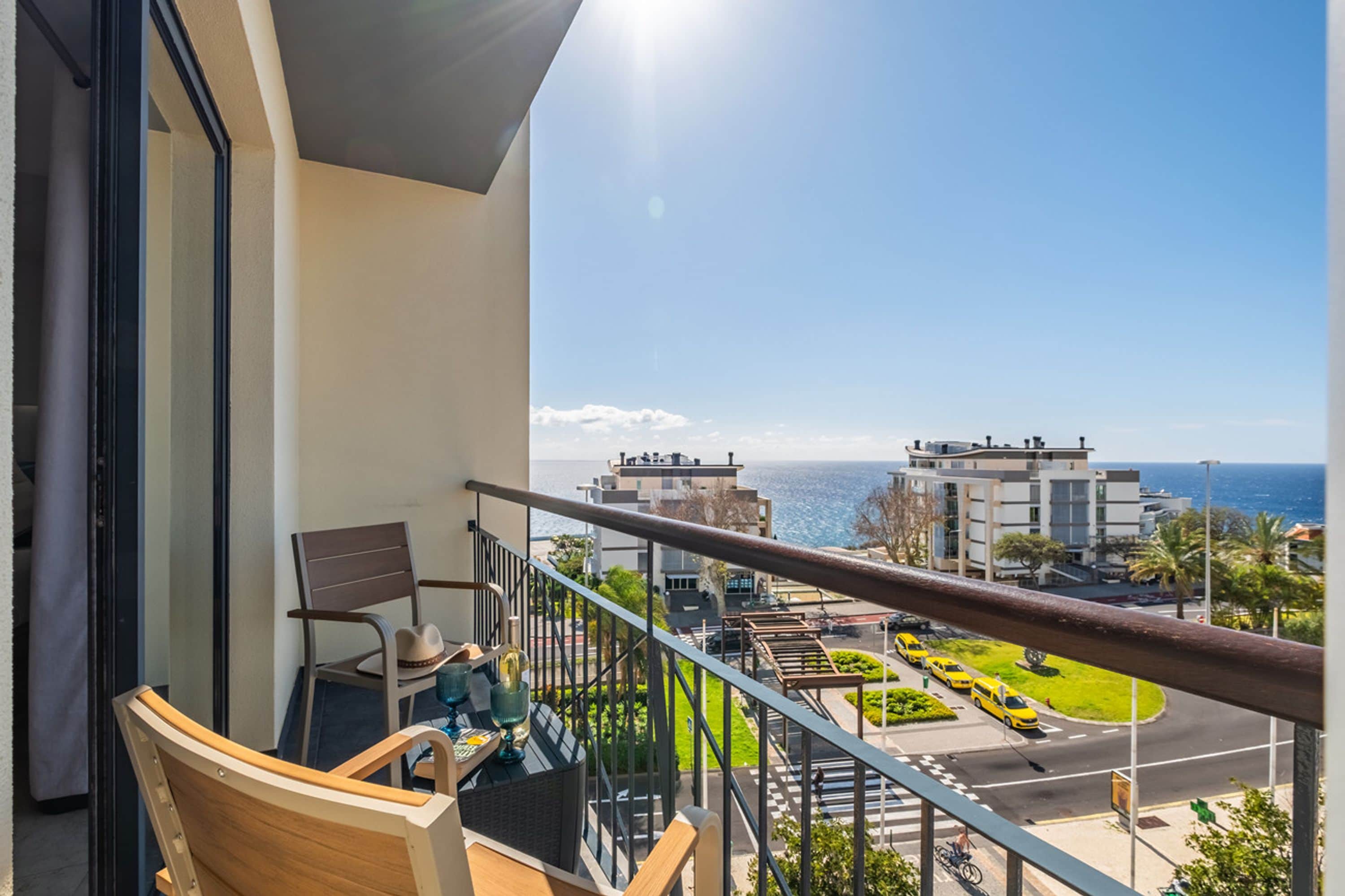 Un balcón con vista al mar, una silla, una mesa con un sombrero y una puerta de cristal.