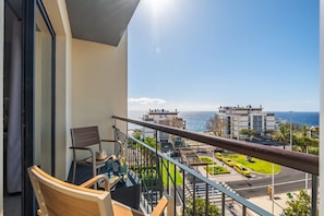A balcony with a view of the sea, a chair, a table with a hat, and a glass door.