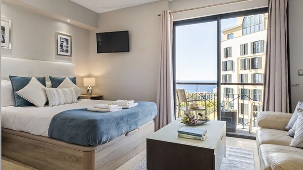 Una habitación de hotel moderna con una cama grande, un televisor de pantalla plana, un balcón con vistas a la ciudad y una zona de estar con una mesa de centro.