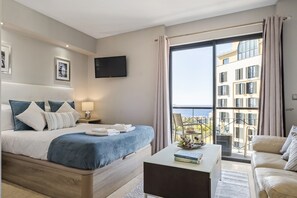 Ett modernt hotellrum med en stor säng, en platt-TV, en balkong med utsikt över staden och en sittgrupp med ett soffbord.
