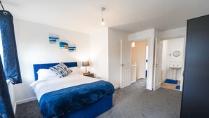 Une chambre à coucher comprenant un lit, une table de chevet, une lampe fixée au mur et une porte donnant sur une salle de bain.