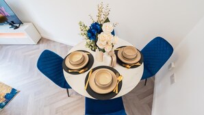 Une table à manger avec quatre couverts en porcelaine noire et dorée, des chaises à revêtement bleu et un vase rempli de fleurs.