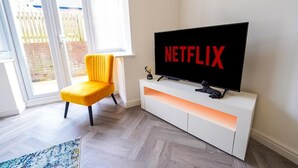 Un salon moderne doté d’un grand téléviseur à écran plat affichant le logo « NETFLIX », d’un fauteuil jaune et d’un meuble de rangement blanc.