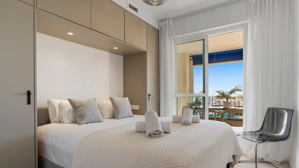 Ein Hotelzimmer mit einem großen Bett, einem Sessel und Blick auf den Pool und die Gebäude.