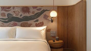 A neatly made bed with white linens, a wall-mounted lamp, and a small wooden nightstand with a remote control.