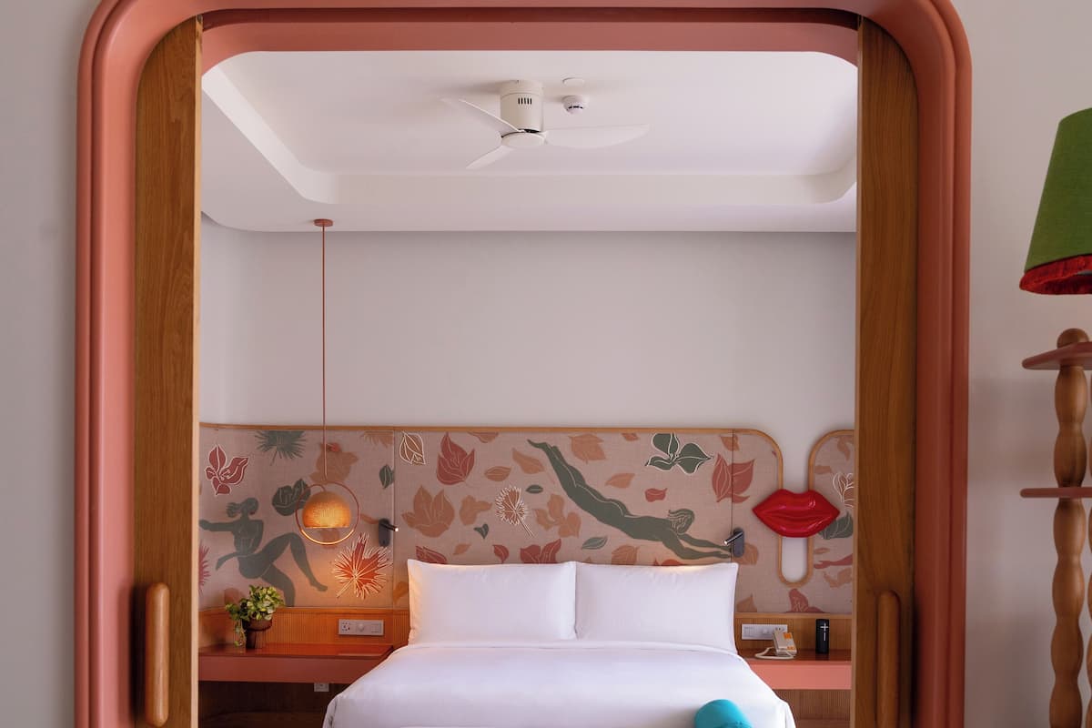 Un dormitorio con cama, mesita de noche, lámpara y una pared con estampado floral.