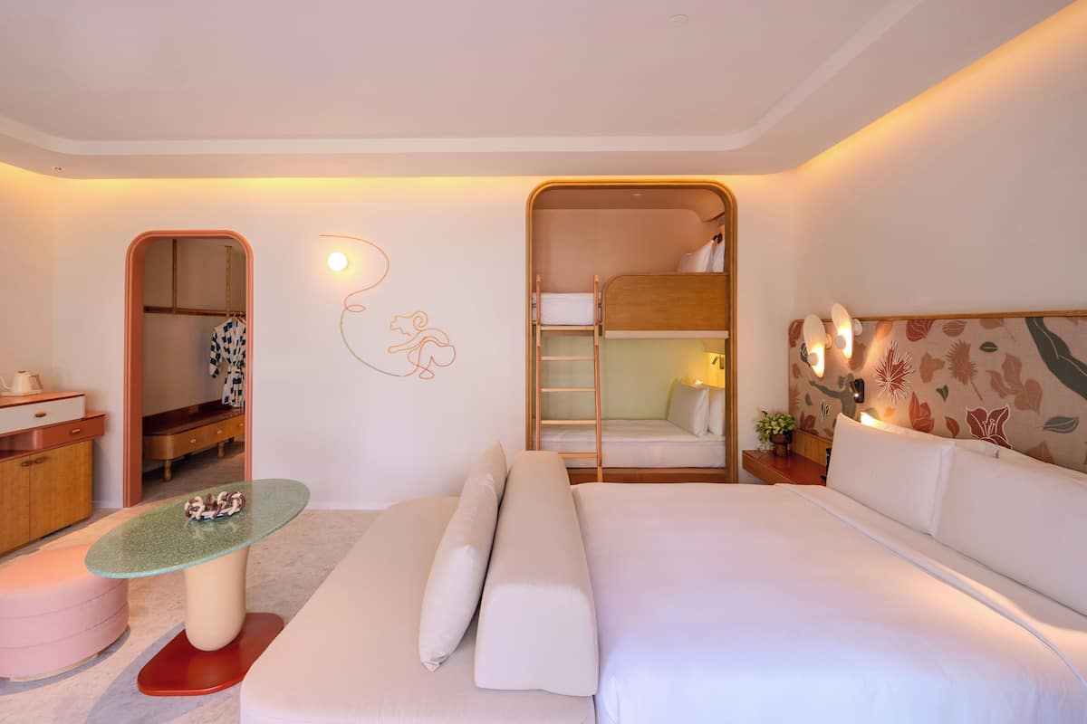 Una habitación de hotel moderna con literas, una kitchenette pequeña, una mesa con cubierta de vidrio y una zona de estar acogedora.
