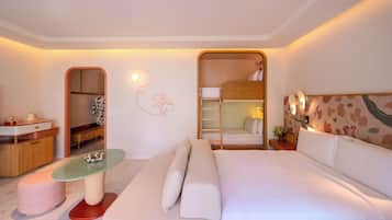 A modern hotel room with a bunk bed, a small kitchenette, a glass-top table, and a cozy seating area.