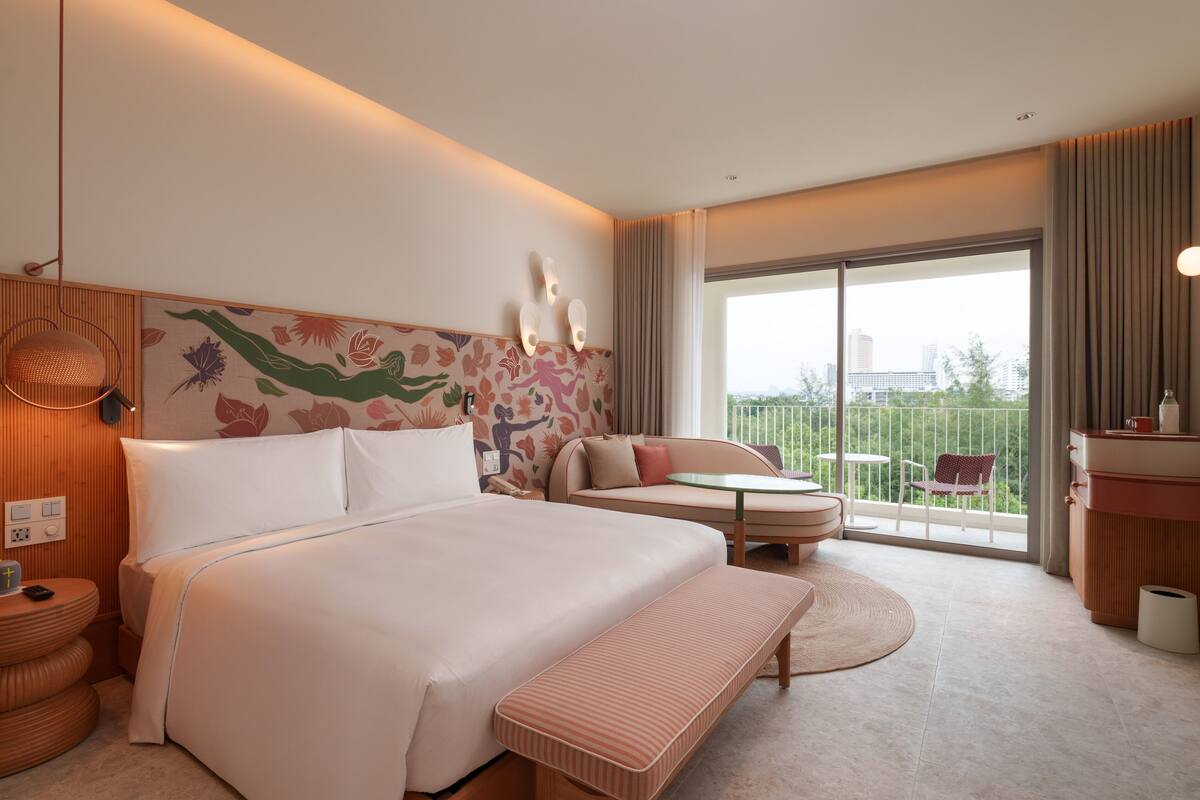Habitación de hotel con una cama grande, un sofá, una mesita, un balcón con vistas a la ciudad y un baño con tocador.