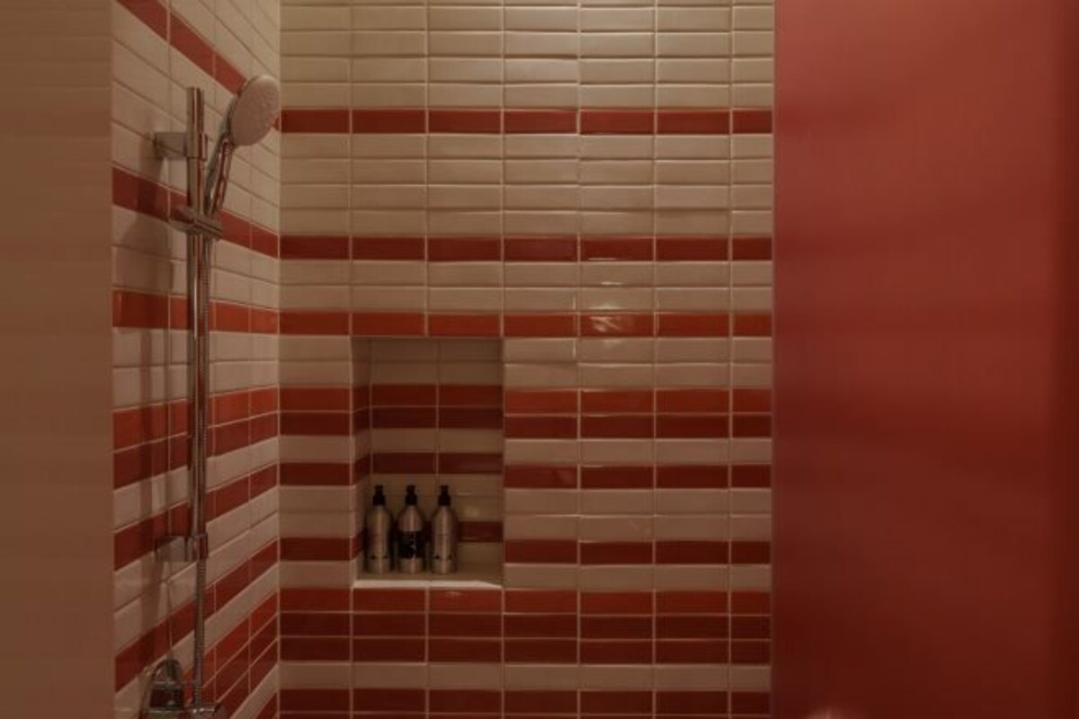 Une salle de bain avec des murs carrelés en rouge et blanc, un espace douche et une étagère contenant des articles de toilette.
