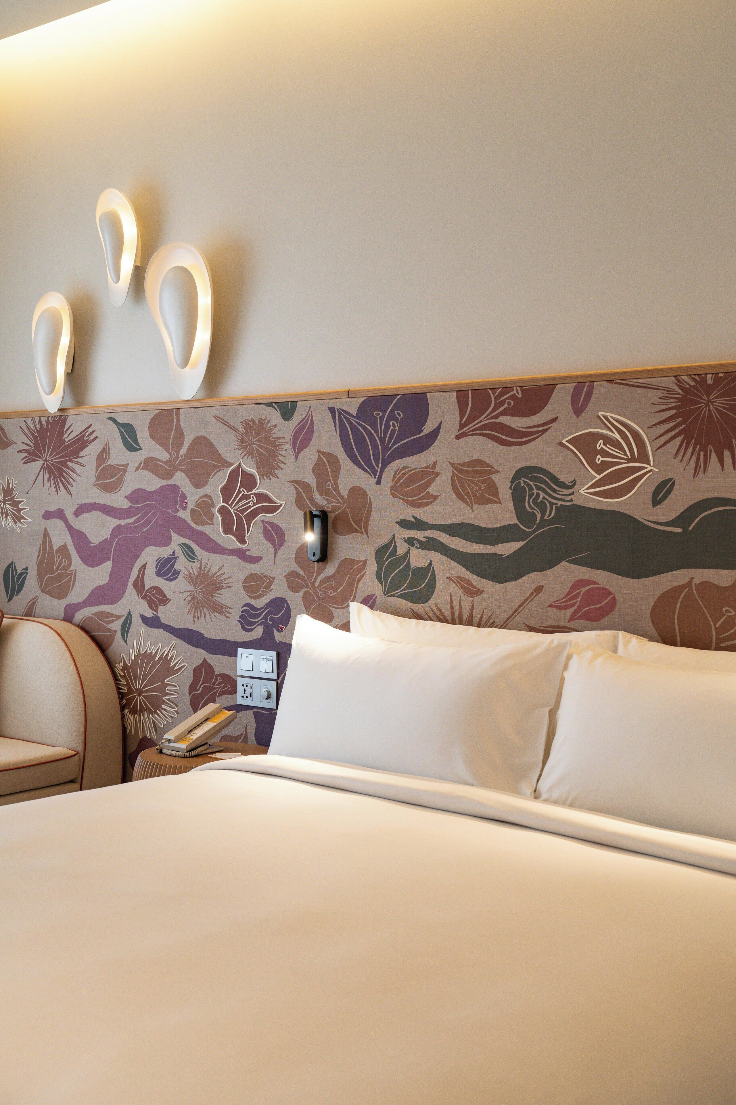Ett hotellrum med en säng, en stol och en vägg med ett blommönster.