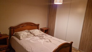En snyggt bäddad säng med ett blommigt sängöverkast, ett träbord vid sängen och en sänglampa.