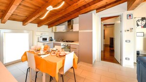 Une cuisine moderne avec des poutres en bois, un coin repas avec des nappes orange et une vue sur une autre pièce.
