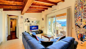 Un salon avec un canapé bleu, un téléviseur diffusant la chaîne « Sky News », et un balcon offrant une vue sur la mer.