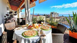 Un espace extérieur aménagé pour prendre les repas, avec deux pizzas, des boissons et des chaises en osier.
