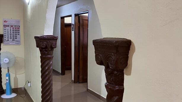 Un couloir avec deux colonnes en bois, un ventilateur de plafond et une porte au fond.