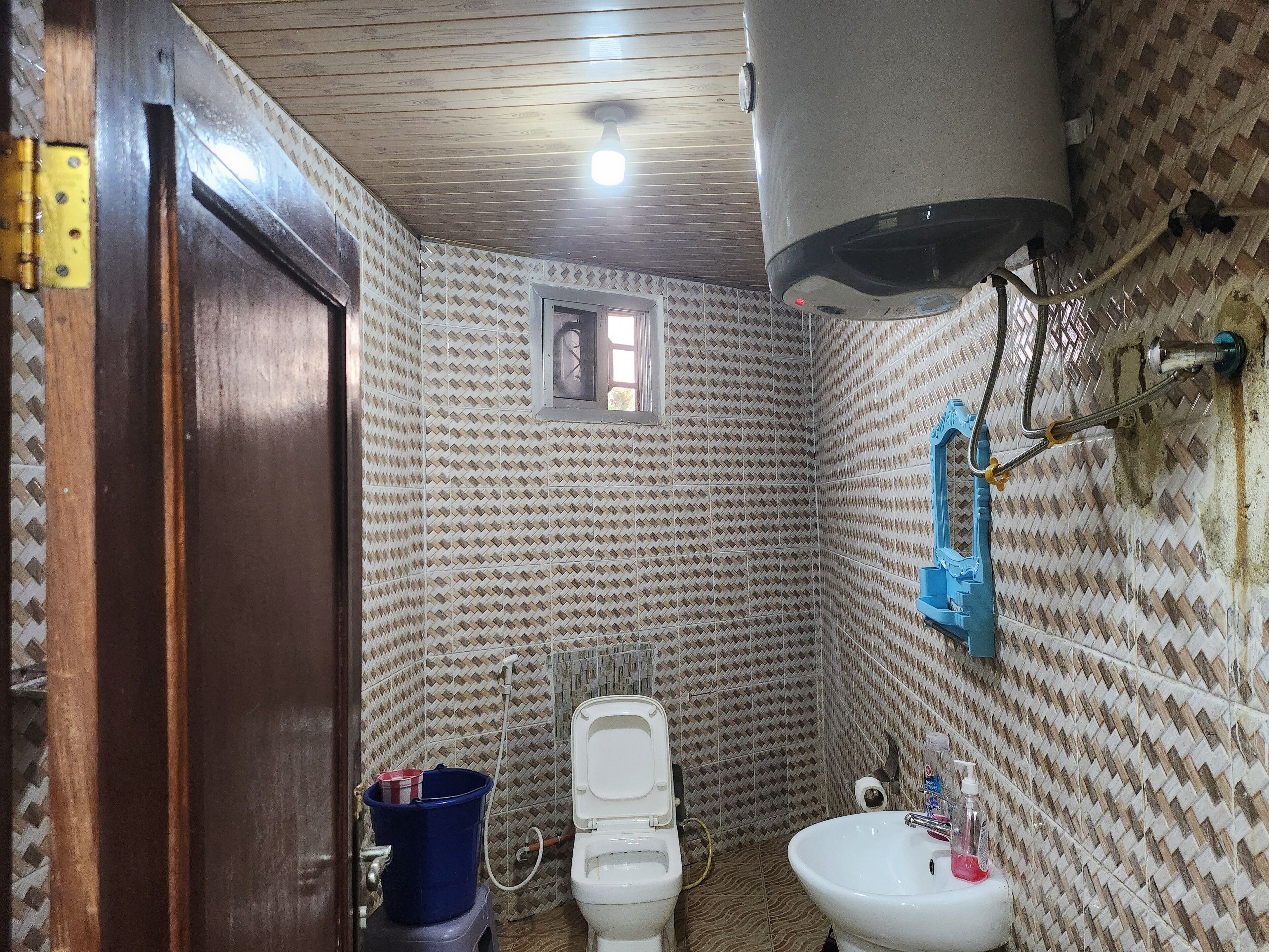 A bathroom with patterned tiles, a toilet, a sink, and a blue bucket.