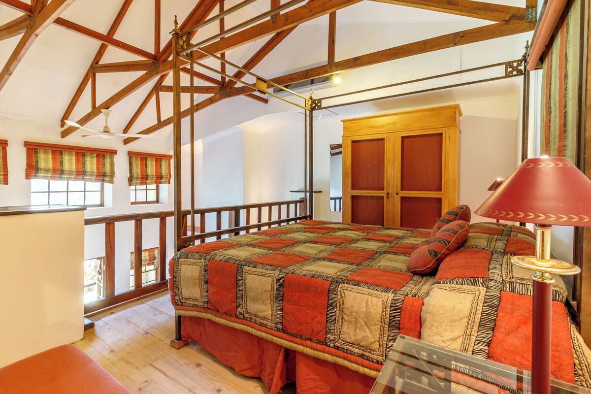 A bedroom with a wooden ceiling, a large bed with a quilt, a wooden wardrobe, and a window with curtains.