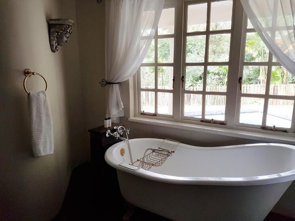 A bathroom with a freestanding bathtub, a towel rack, and a window with curtains.