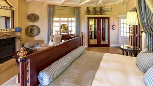 Un dormitorio amplio con una cama grande, un banco de madera, una chimenea y un ventilador de techo.