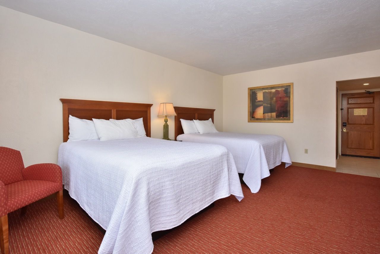 Habitación de hotel con dos camas, un sillón rojo, un cuadro en la pared y una puerta de madera.