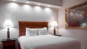 Habitación de hotel con una cama grande, dos mesitas de noche con lámparas, un cuadro en la pared e iluminación empotrada en el techo.