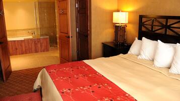 A hotel room with a bed, a nightstand with a lamp, a wooden headboard, a bathroom with a mirror and sink, and a door leading to the bathroom.
