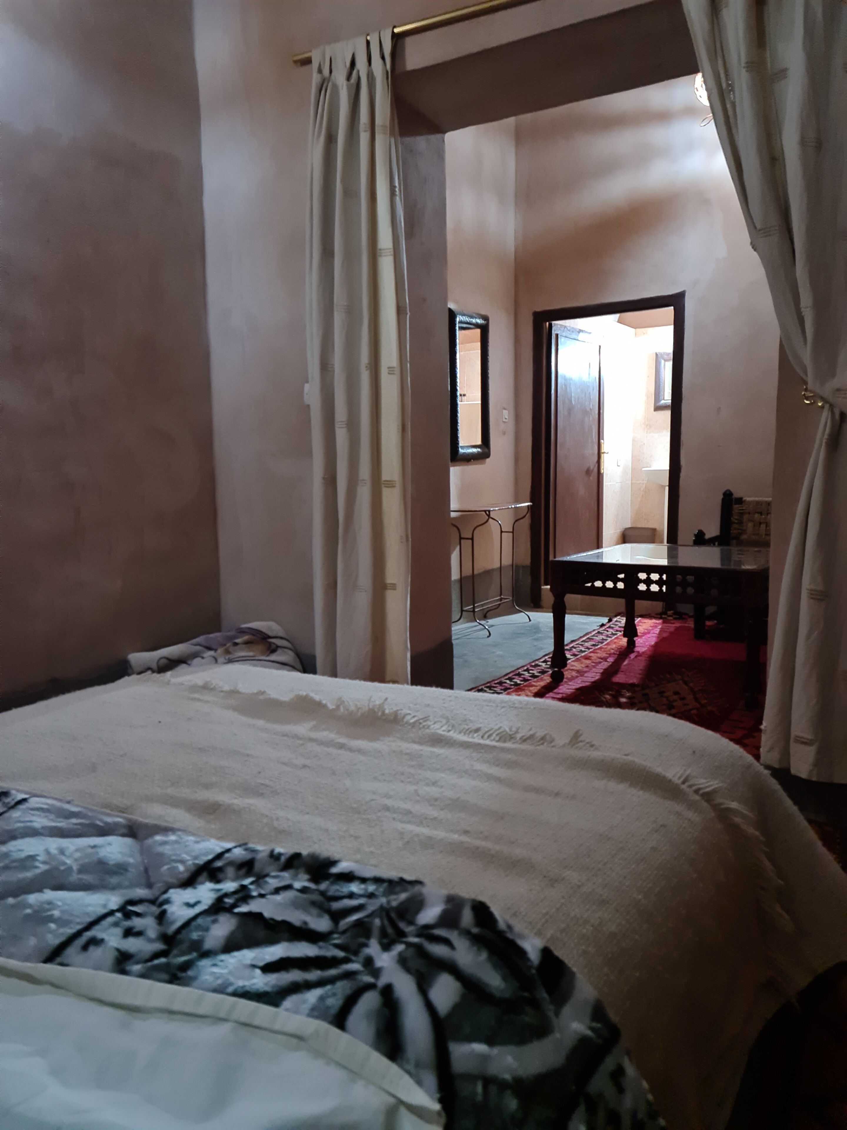 Un dormitorio con cama, una silla, una mesita y un espejo en la pared.