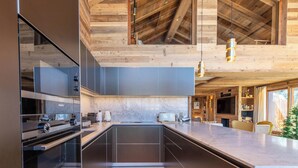 A modern kitchen with a large island, built-in appliances, and a wooden ceiling.
