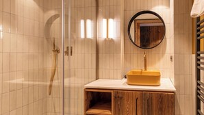 A modern bathroom with a glass-enclosed shower, a wooden vanity with a yellow sink, and a round mirror.