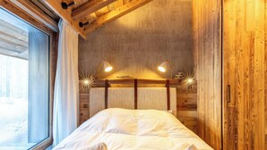 A cozy wooden room with a bed, two bedside lamps, and a window.