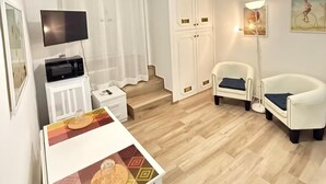 A modern, well-lit living room with a ceiling fan, a flat-screen TV, a dining table with a patterned tablecloth, two white armchairs, and a floor lamp. - Best Bnb Alfieri (Florence)