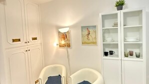 A room with two white armchairs with blue cushions, a white cabinet with glass doors, and a wall-mounted lamp. - Best Bnb Alfieri (Florence)