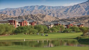 A golf course with a pond, surrounded by red-roofed buildings and mountains in the background. - WorldMark Indio, 2 Bedroom/2 Bath Condo for Coachella (Indio)
